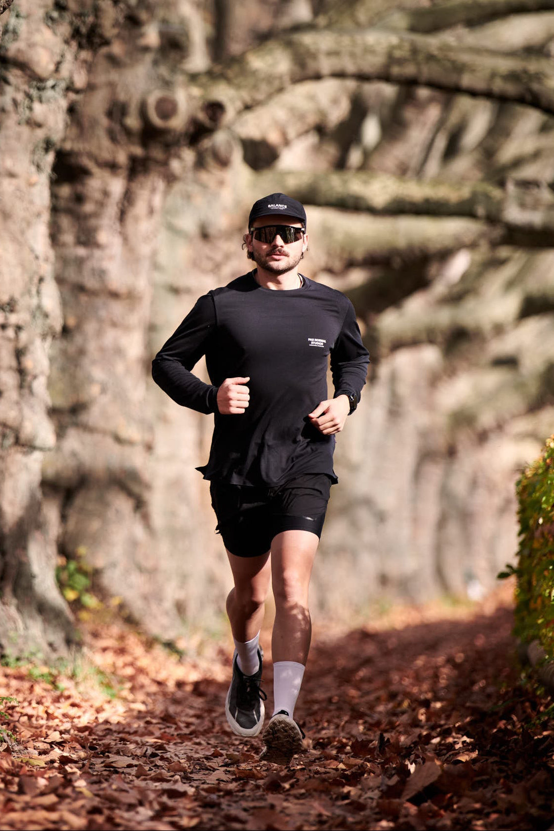 Person running through a forest with large trees and fallen leaves on the ground.