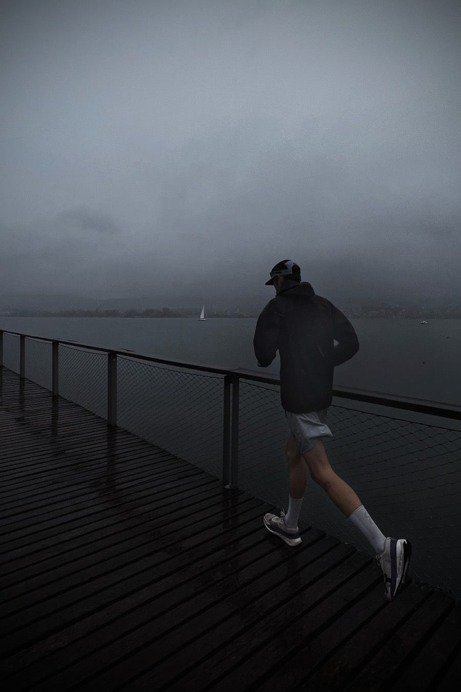 A runner on a wet wooden pier along Lake Zurich in the rain