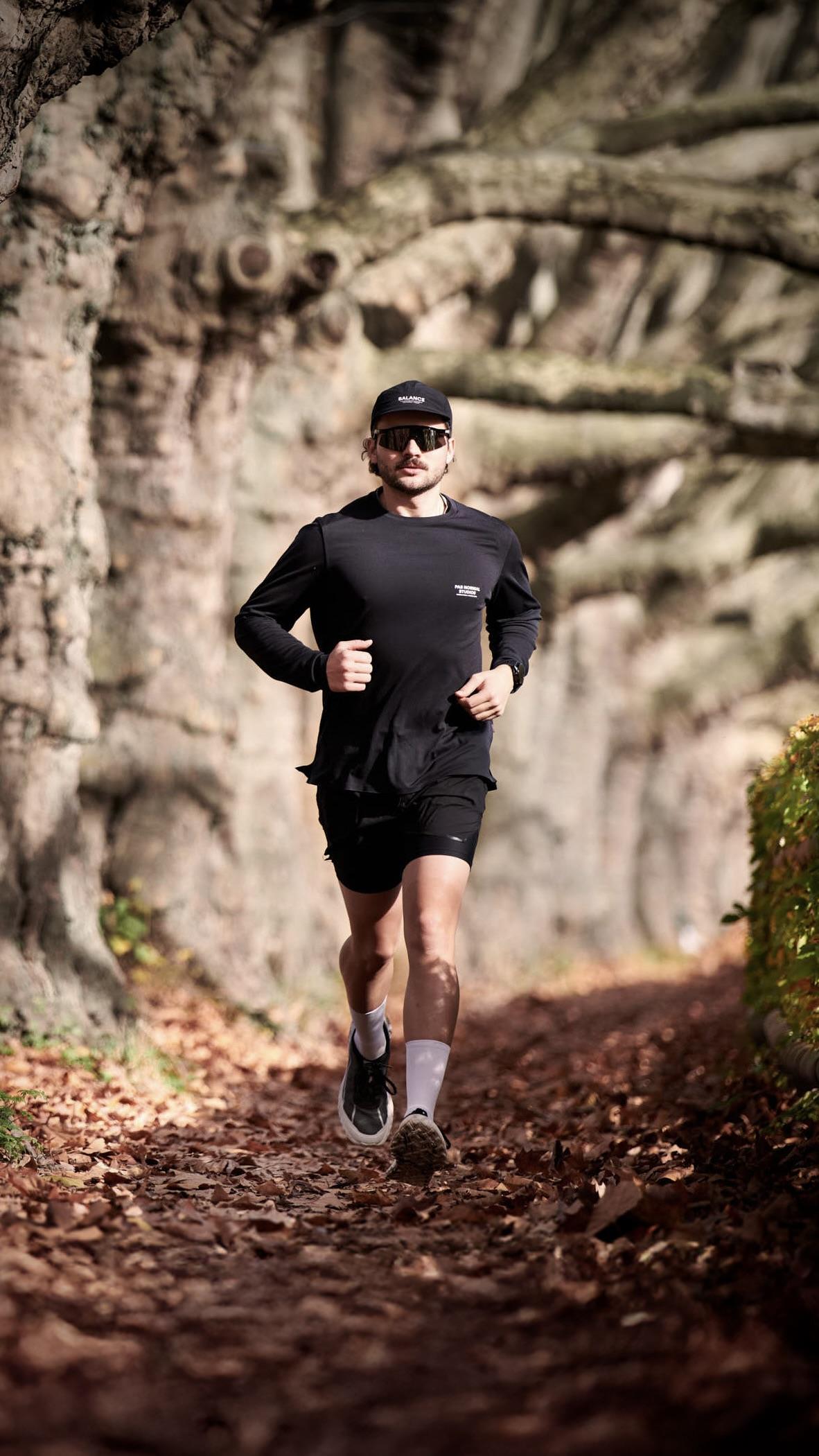 Runner in black on a leaf covered path under old plane trees